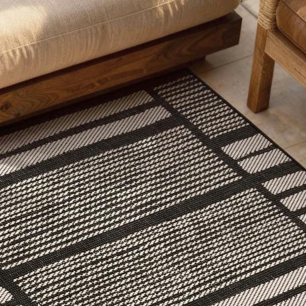 Black and white striped rug on a wooden floor with a beige sofa and wooden chair.