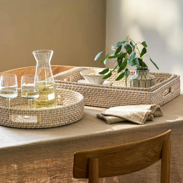A variety of round and rectangular whitewash rattan trays styled together on a linen-covered table.