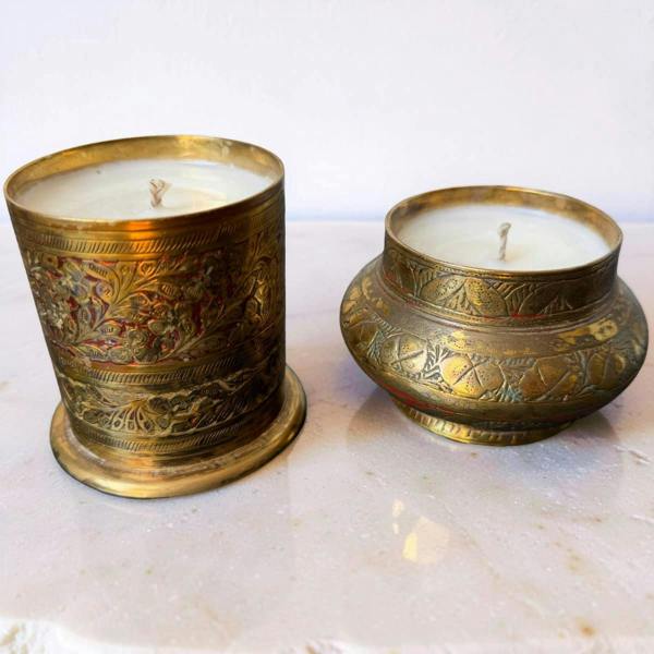 Two ornate brass candle holders with candles on a marble surface.