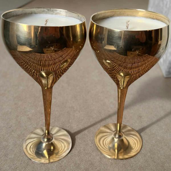 Two gold candle holders with candles inside on a neutral background
