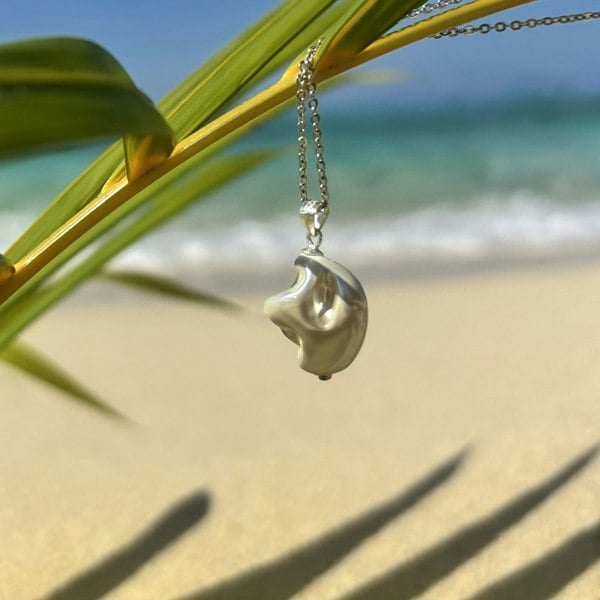 Sterling silver pendant charm featuring natural shell in silver colour, shot on an exotic castaway beach.
