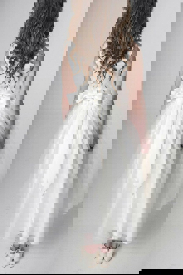 Ivory flower girl dress with a bow on a plain background