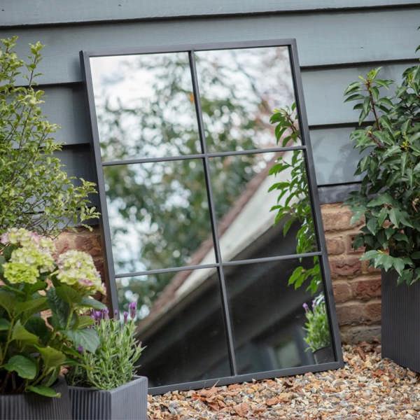 The 100x70cm rectangular black metal window pane mirror mounted horizontally on a white garden brick wall by Abode Home & Gifts.
