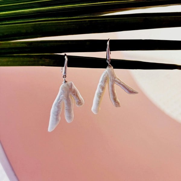 Silver earrings featuring large, irregular baroque pearls hanging off a palm leaf.