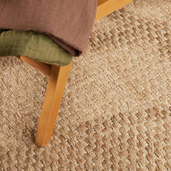 Close-up of a textured beige carpet with a wooden chair leg and green cushion.