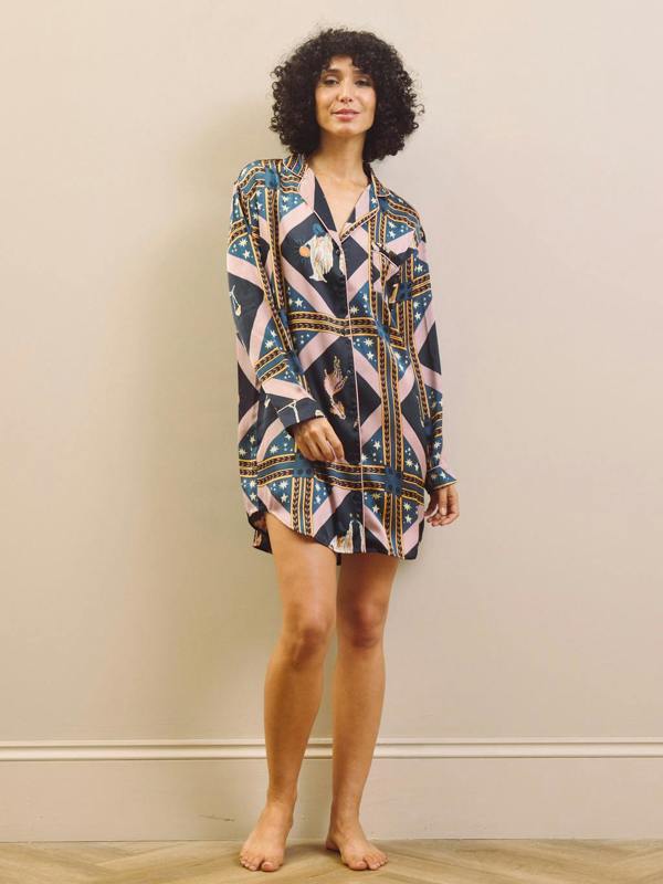 Woman wearing a patterned night dress standing against a plain wall.