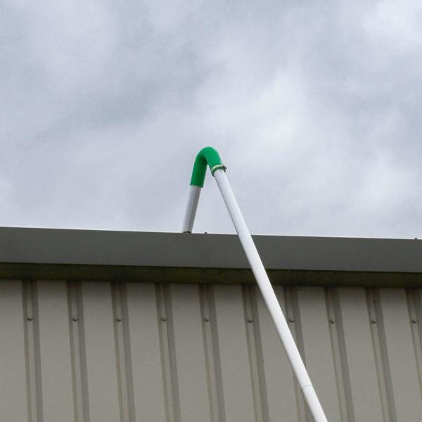 Gutter vacuum poles with a green bend, extending over a gray metal roof, designed for efficient cleaning of gutters