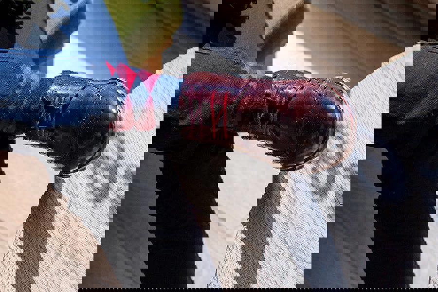 Person wearing a dark shoe and red and black diamond design sock on a wooden floor.