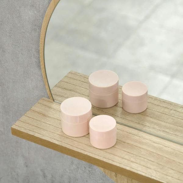 Round mirror with natural wood-effect shelf holding pink skincare jars