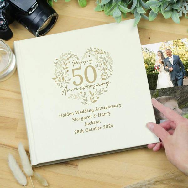 An ivory square photo album from Abode Home & Gifts printed with 'Golden Wedding Anniversary Margaret & Harry Jackson' on a wooden surface.