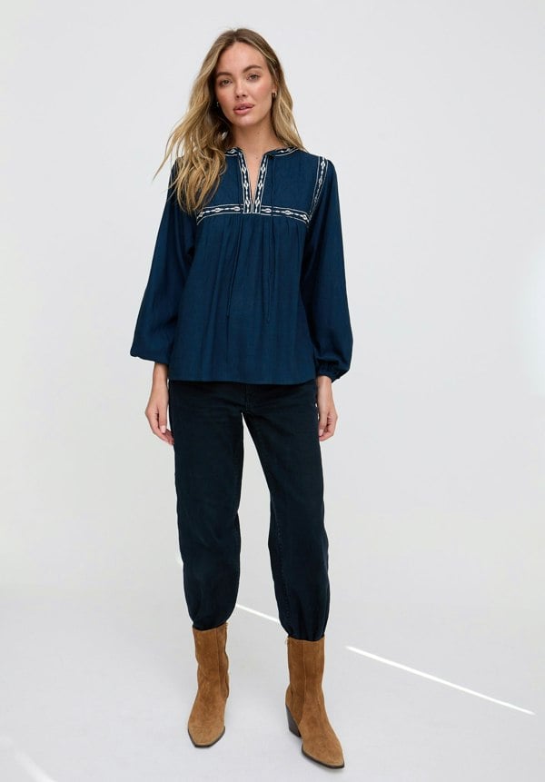 Woman wearing a dark blue blouse and black pants with brown boots on a white background