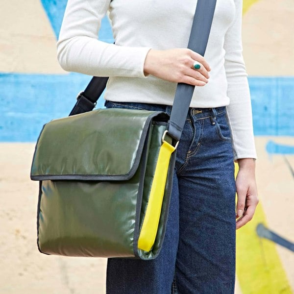 A woman wearing jeans and a green Recycled Plastic and Seat Belt Messenger Bag made from recycled plastic.