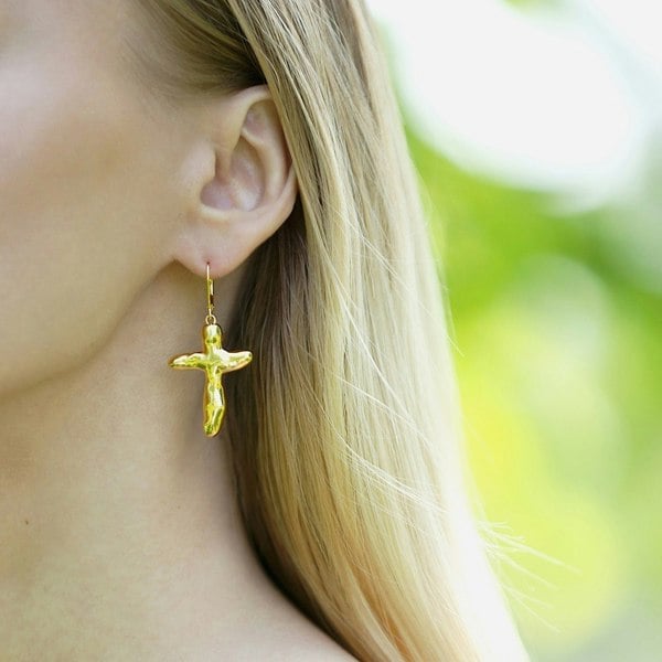 Close up of an ear with gold vermeil cross earring.