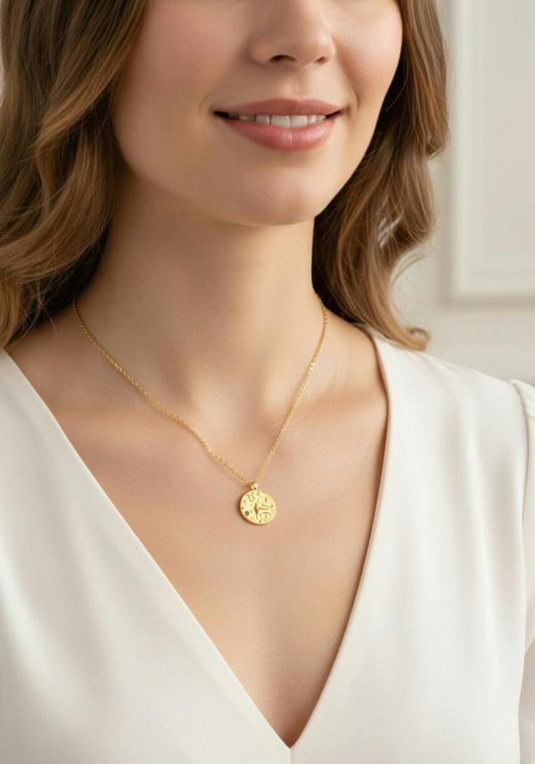 Woman wearing a gold necklace with a round pendant against a neutral background