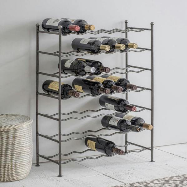 A tall, freestanding industrial black steel wine rack with empty zig-zag wire bottle slots arranged in 7 rows.