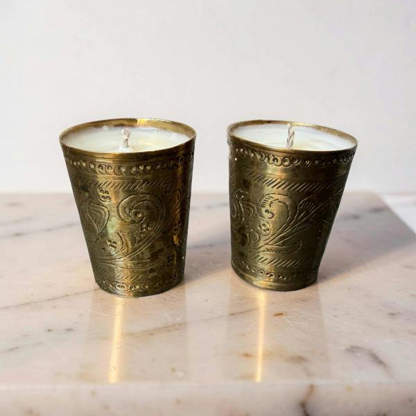 Two ornate brass candle holders with candles on a marble surface.