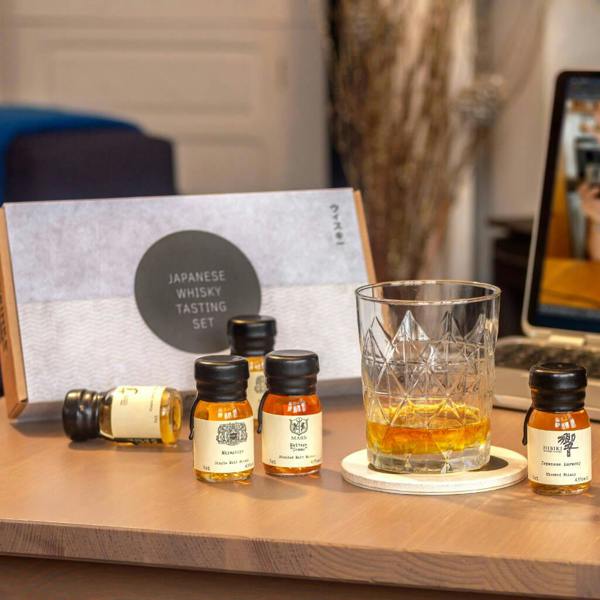 Five miniature 3cl wax-sealed bottles from a Japanese Whisky Tasting Set displayed on a wooden desk next to a crystal tumbler glass and its presentation gift box.