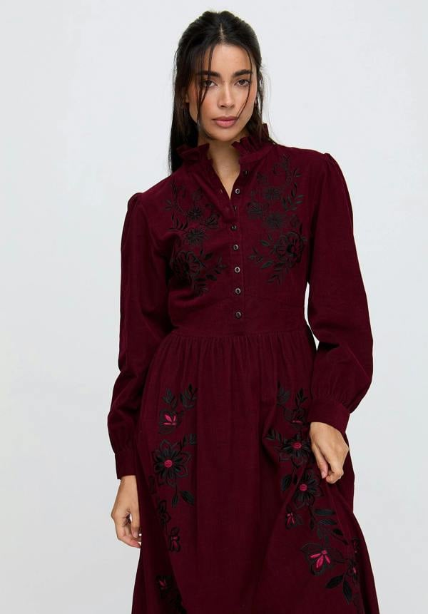 Woman wearing a burgundy dress with floral embroidery on a white background