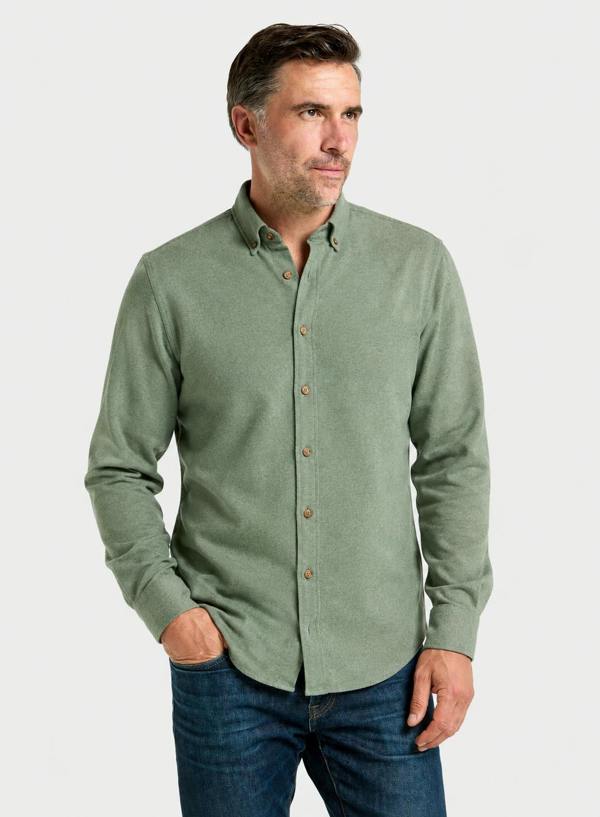 A man wearing a sage green long-sleeve button-down shirt and blue jeans, standing against a light gray studio background.