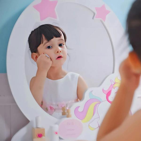 Young child looking into oval unicorn mirror on pink kids dressing table