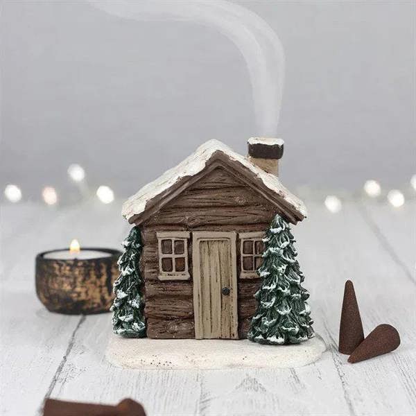 Log cabin incense cone burner with incense cone, pine trees, and lit candle nearby