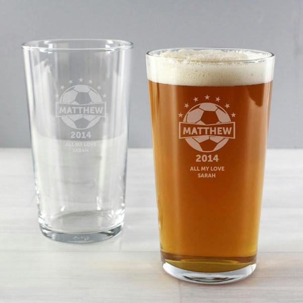 An engraved Name And Year Football Pint Glass filled with a frothy amber beer next to an empty duplicate glass showing the frosted crest design.