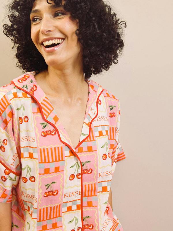 Woman wearing a colourful cherry patterned pyjama top with a neutral background