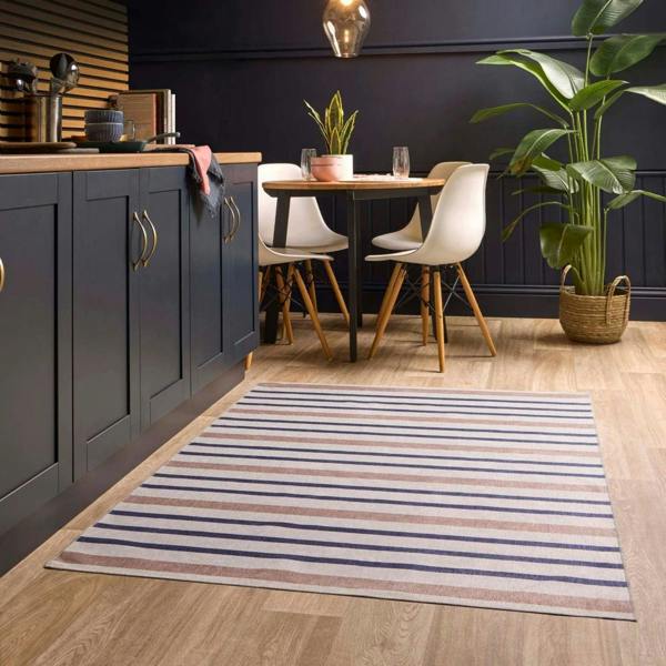 Modern kitchen with dark blue cabinets, wooden dining table, and striped rug.