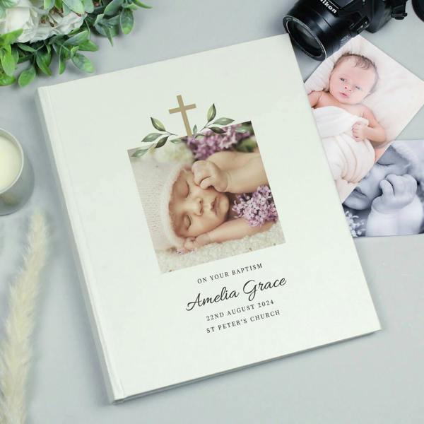 An ivory satin christening photo album from Abode Home & Gifts printed with 'Amelia Grace' and a custom baby picture on a grey desk.