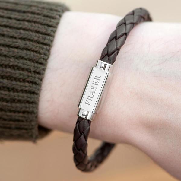 Personalised men's brown braided leather bracelet worn on a wrist, featuring a stainless steel plate engraved with FRASER