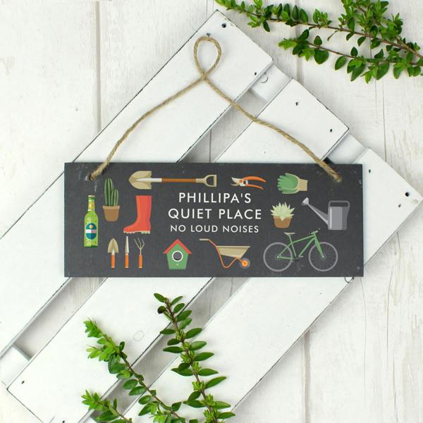 A rectangular hand-cut dark slate hanging sign featuring natural string, colourful garden illustrations, and custom uppercase text reading Phillipa's Quiet Place No Loud Noises.