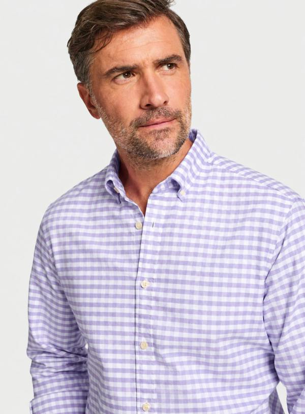 A man wearing a light purple and white gingham button-down shirt, shown from the chest up against a plain light gray studio background.