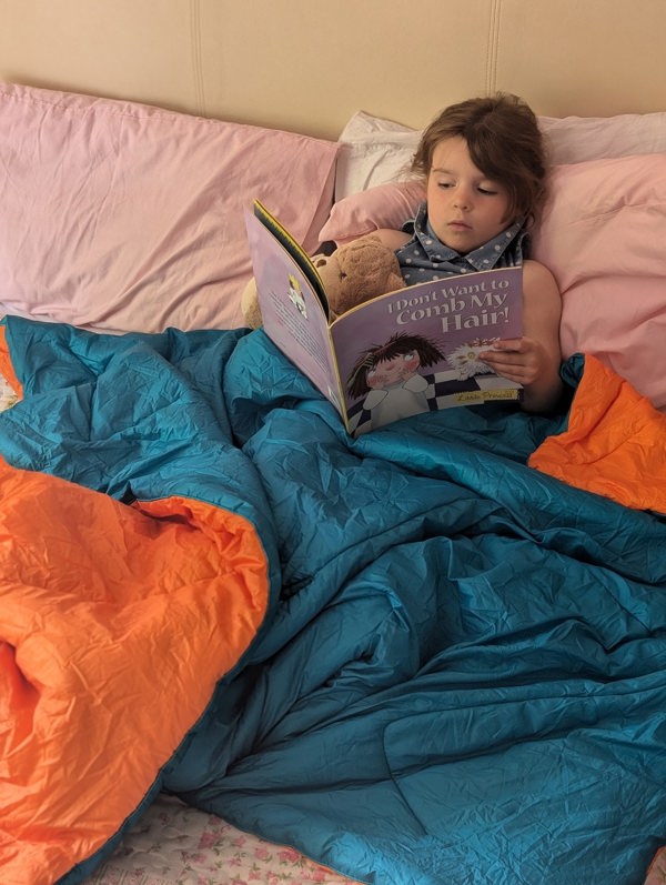 A child in sat up in bed with Insulated Reversible Blanko by OLPRO over them reading a book.