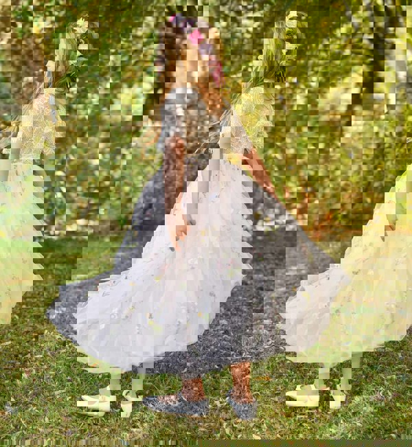 Young girl in a floral dress standing outdoors with greenery in the background
