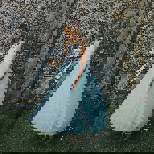 Young girl in a light blue dress standing against a stone wall.