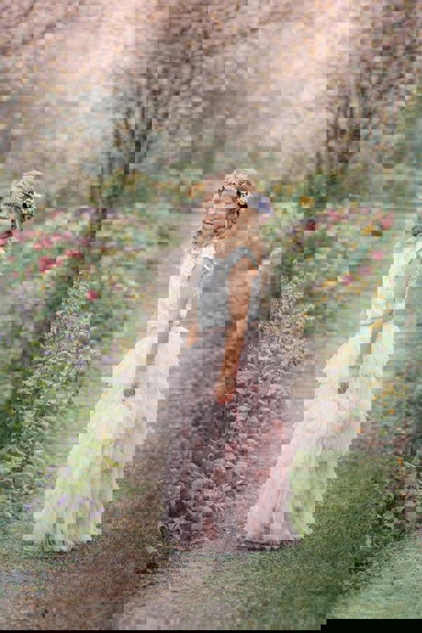 Young girl in a white top and pink tulle skirt standing in a garden with cherry blossoms.
