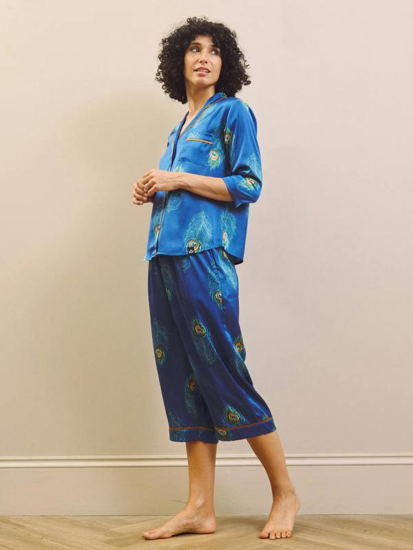 Woman wearing a blue pajama set with floral patterns against a beige wall.