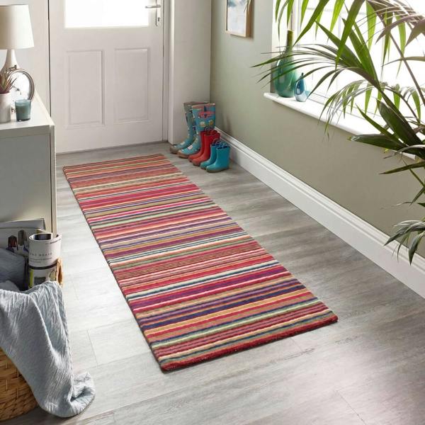 Colorful striped rug on a wooden floor with a white door and plant in the background