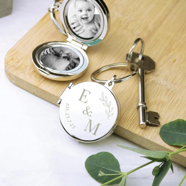Personalised Foliage Couples Photo Keyring engraved with E & M and date, shown open with two photos inside on a wooden board.