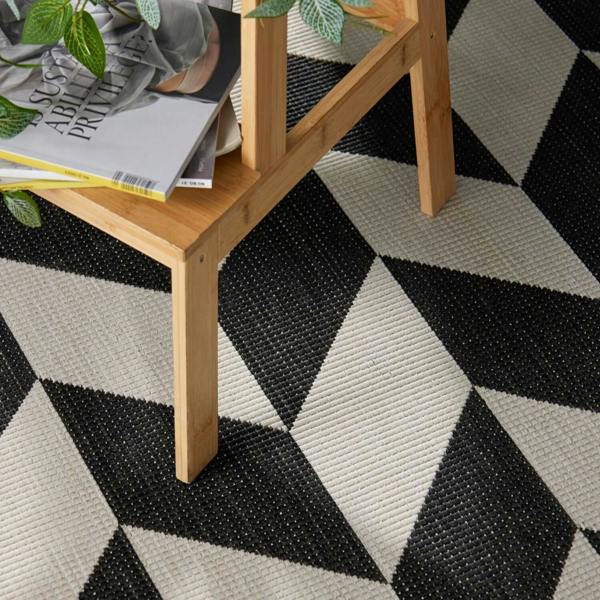 Black and white geometric patterned rug with a wooden side table and books on top.