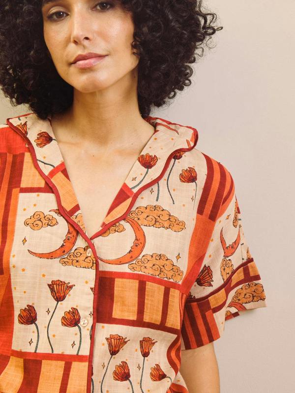 Woman wearing a rust and cream patch work patterned pyjama set against a plain wall. Detail