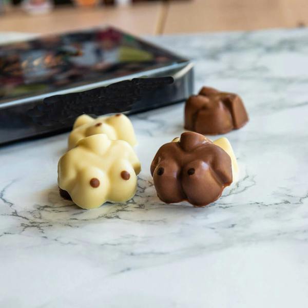 our novelty chocolates shaped like breasts, made from a mix of white and milk Belgian chocolate, displayed on a white marble surface with a gift box in the background.