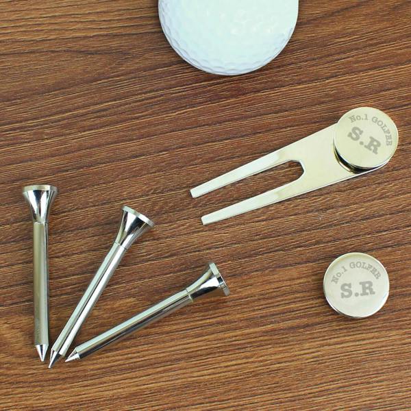 Personalised metallic golf accessory set on a wooden surface showing three silver tees, a pitch repairer, and a round ball marker engraved with initials and No.1 Golfer text.