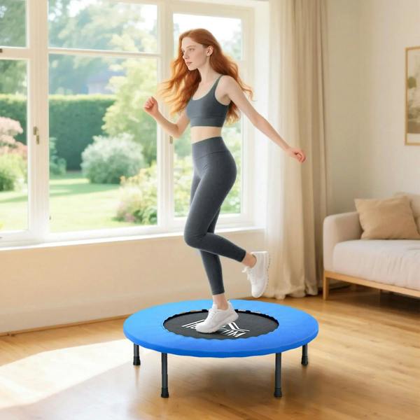 Blue mini trampoline with black jumping surface and safety pad, indoors with a person stepping