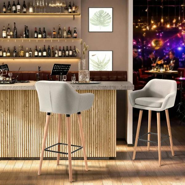 Two beige upholstered bar stools with curved backs, black metal footrests, and light wood legs
