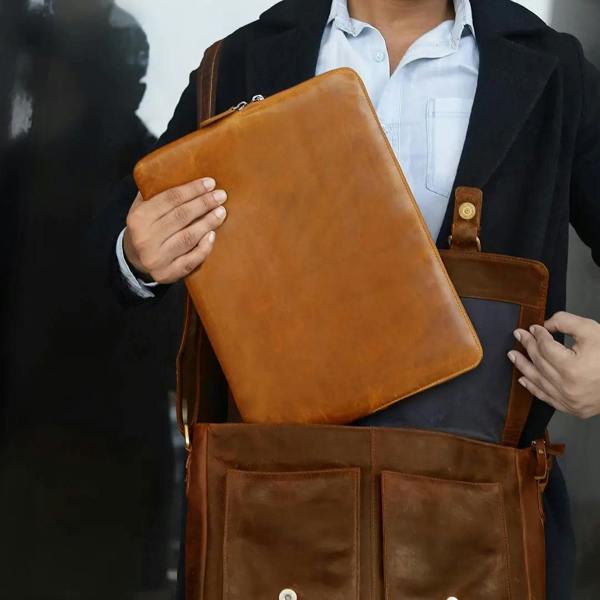 Person holding a tan leather laptop sleeve with a plain background