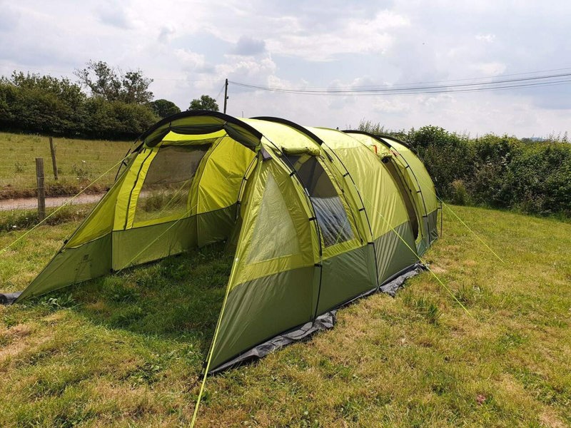 An image of the Abberley XL Extension by Olpro attached to the Abberley XL Tunnel Tent on a camping field with the front open and window blind open.