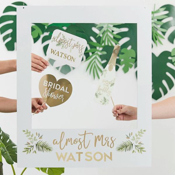 Hands holding a white botanical hen party photo frame personalised with gold text reading almost Mrs WATSON alongside matching handheld photo props.
