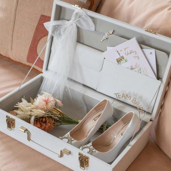 White faux-leather Stackers memory storage trunk open to show wedding shoes, a veil, and cards inside a velvet-lined interior with gold clasps.