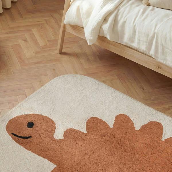 Dinosaur-shaped rug on a wooden floor next to a bed